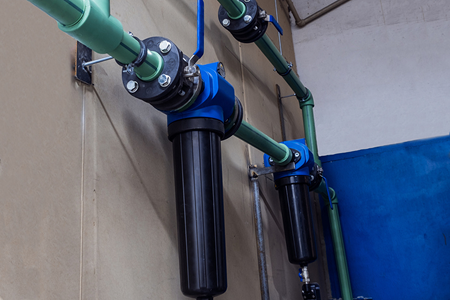 Piping system fastened to a factory wall with filters, flanges, and fittings